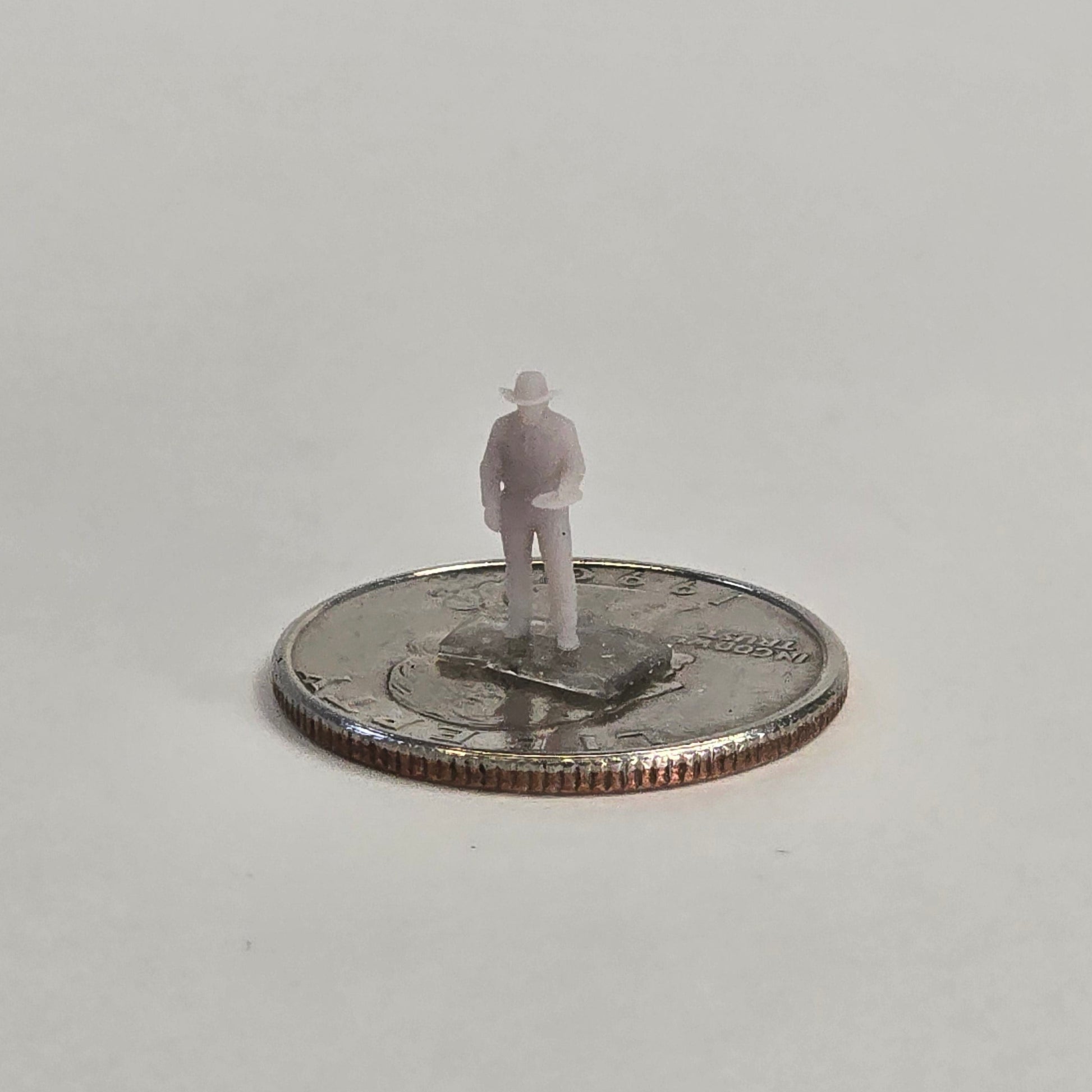 Unpainted N scale cowboy figure holding a dinner plate in his right hand, wearing a hat and standing on a U.S. quarter for scale reference.