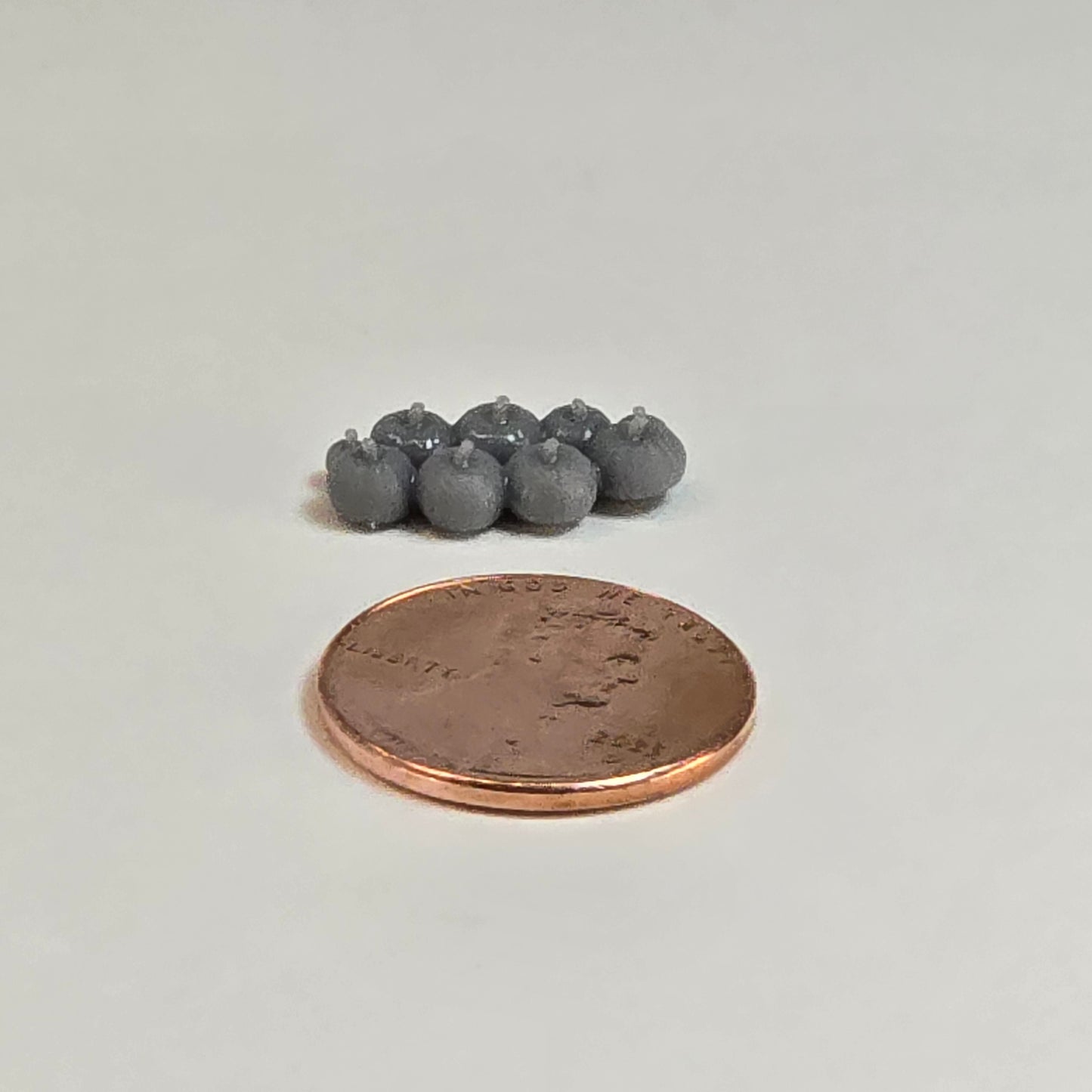 “Eight sculptural grey miniature pumpkins in two rows with a shiny penny for scale, displayed on a neutral background.”