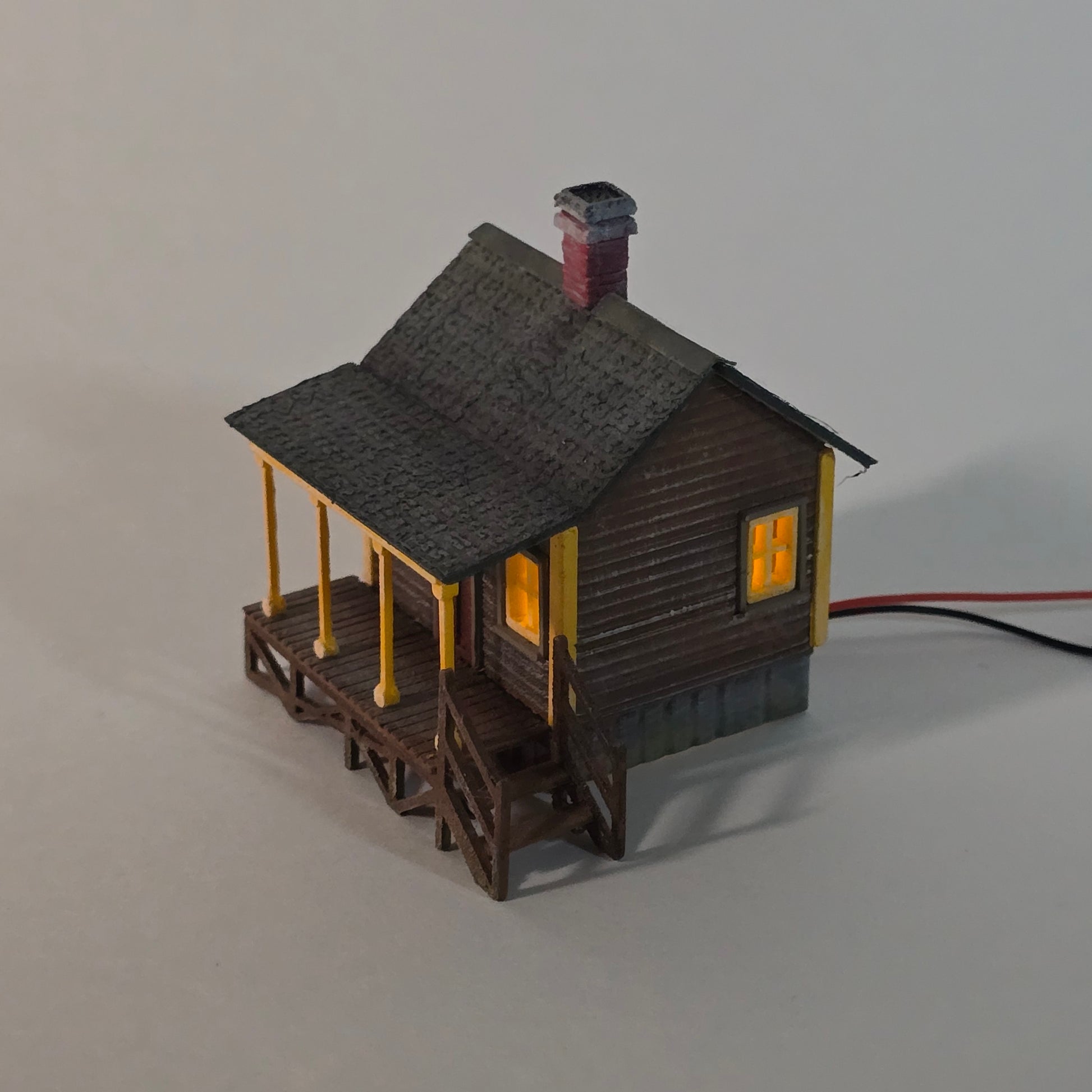 Small model of a house with a gray roof and yellow accents on a plain background